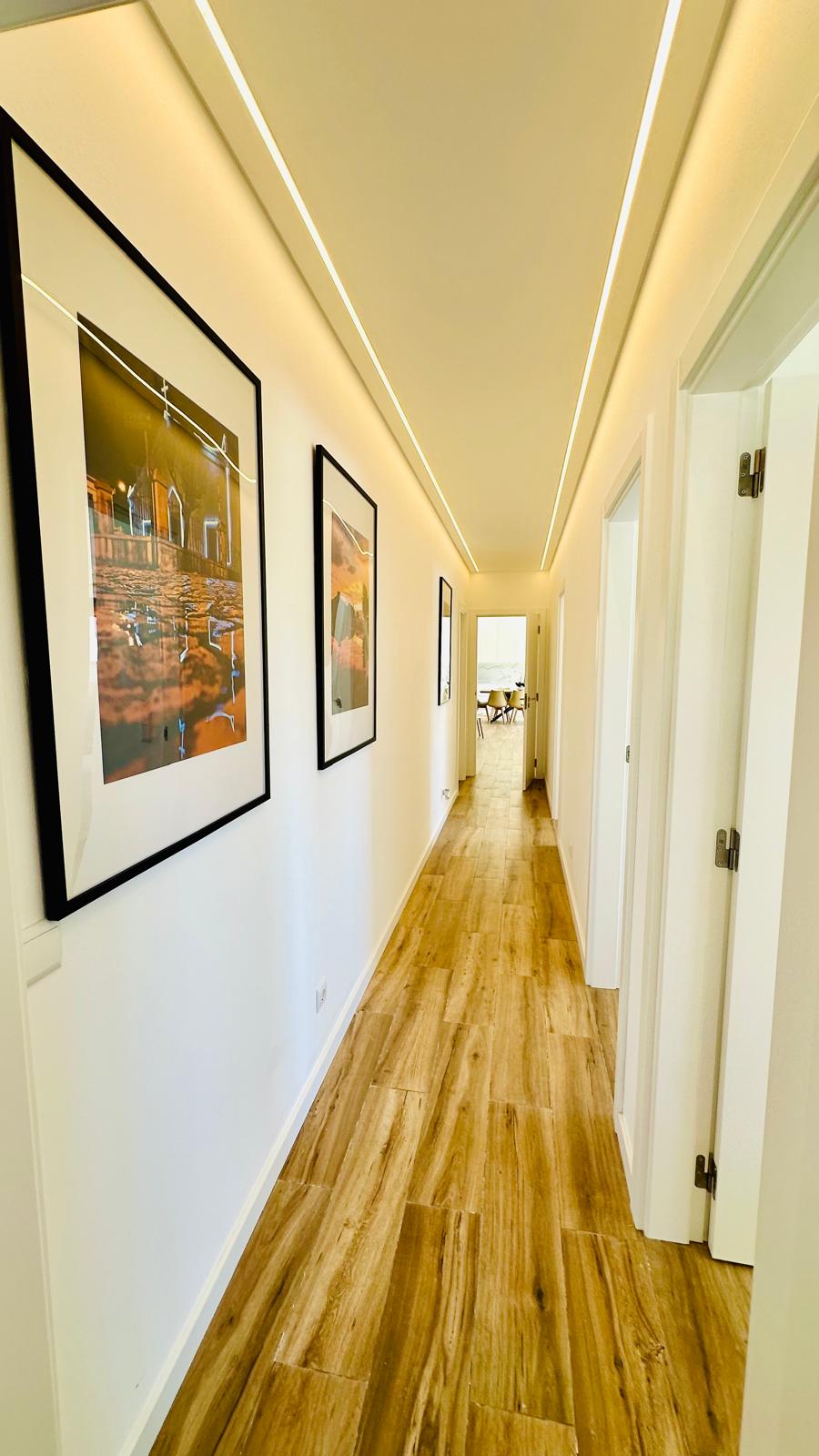 Corredor com pavimento em madeira e luz linear no teto